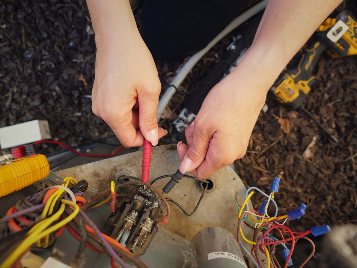 Close-up of hands diagnosing a capacitor with a meter